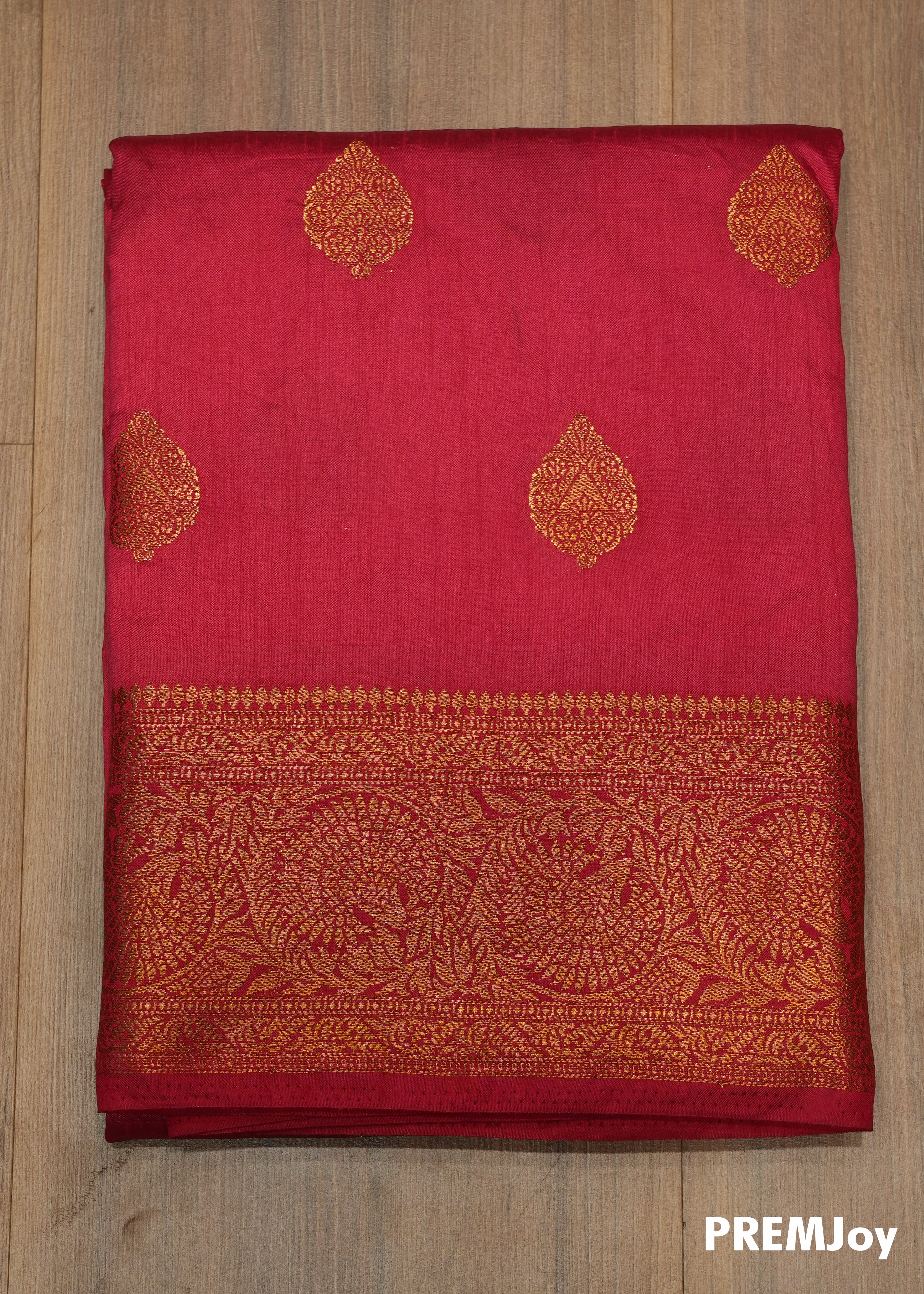 Red saree with gold patterns on a wooden surface, branded 'PREMJOW'.