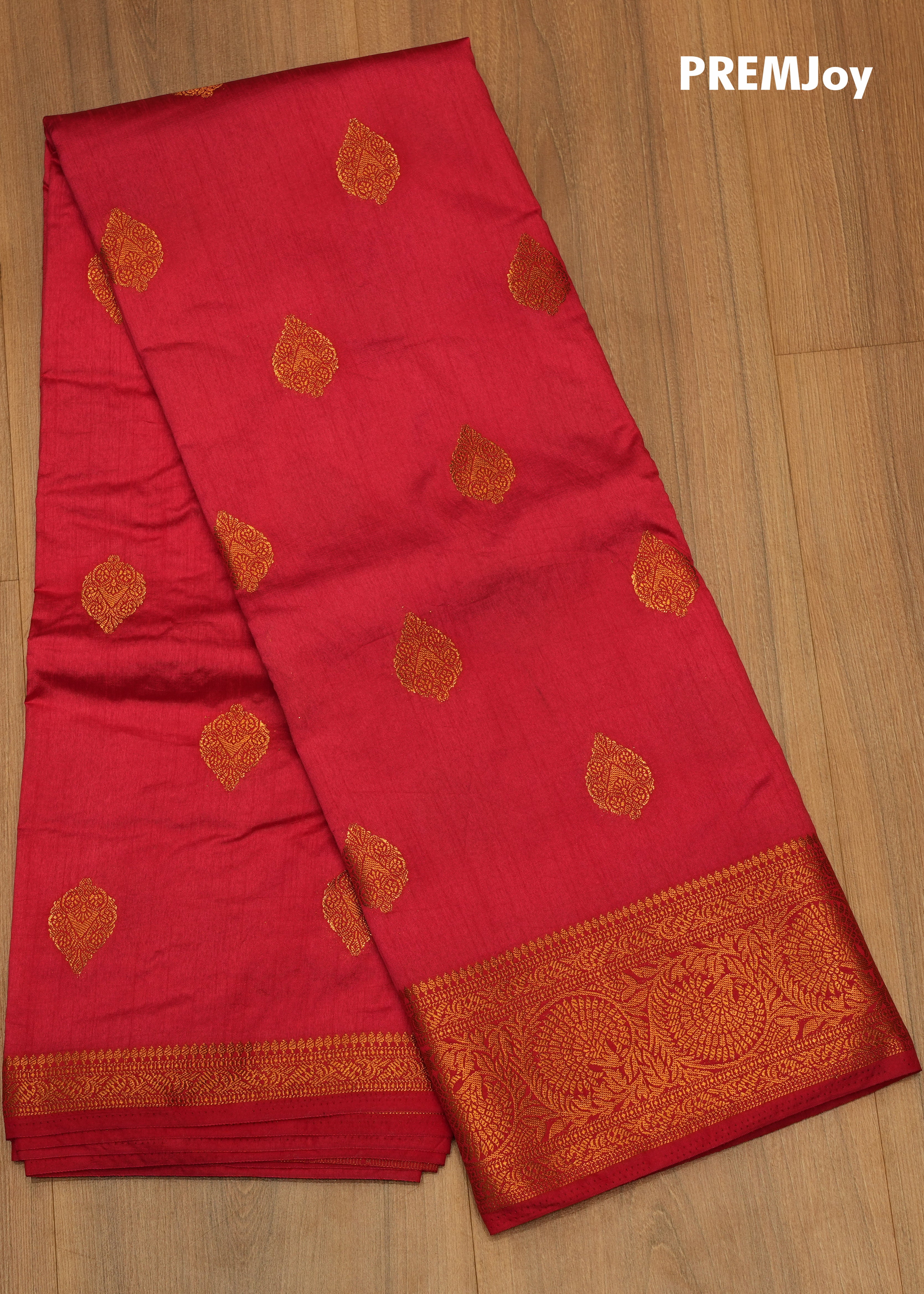 Red saree with gold patterns on a wooden surface, branded 'PREMJoy'.