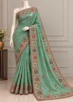 A mint green saree with intricate red, gold, and black floral embroidery, displayed on a white mannequin in an indoor setting with a neutral paneled wall background.